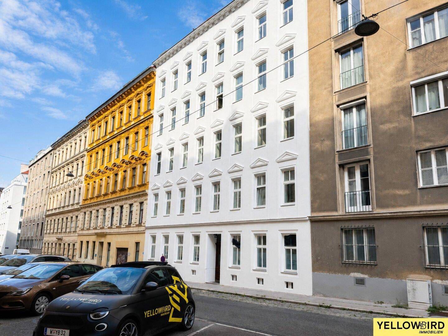 Historisches Gebäude mit klassischer Fassade und parkenden Autos auf der Straße.