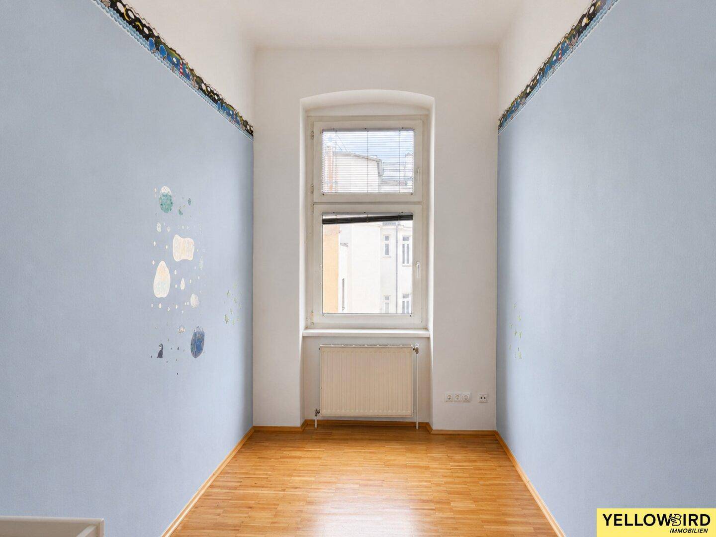 Kleines Zimmer mit Holzfußboden, blauen Wänden und einem Fenster mit Heizkörper.