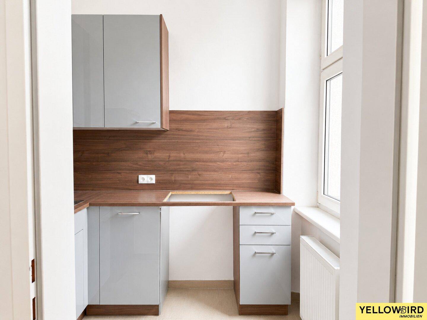 Kompakte Küche mit grauen Schränken, Holzdetails und einem Fenster für Tageslicht.