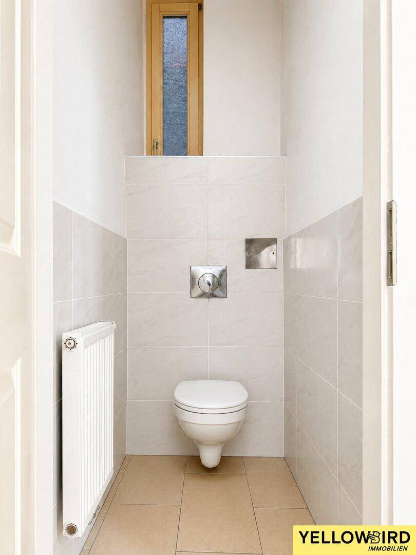 Separates WC mit Wand-WC, Heizkörper und schmalem Fenster für Belüftung.