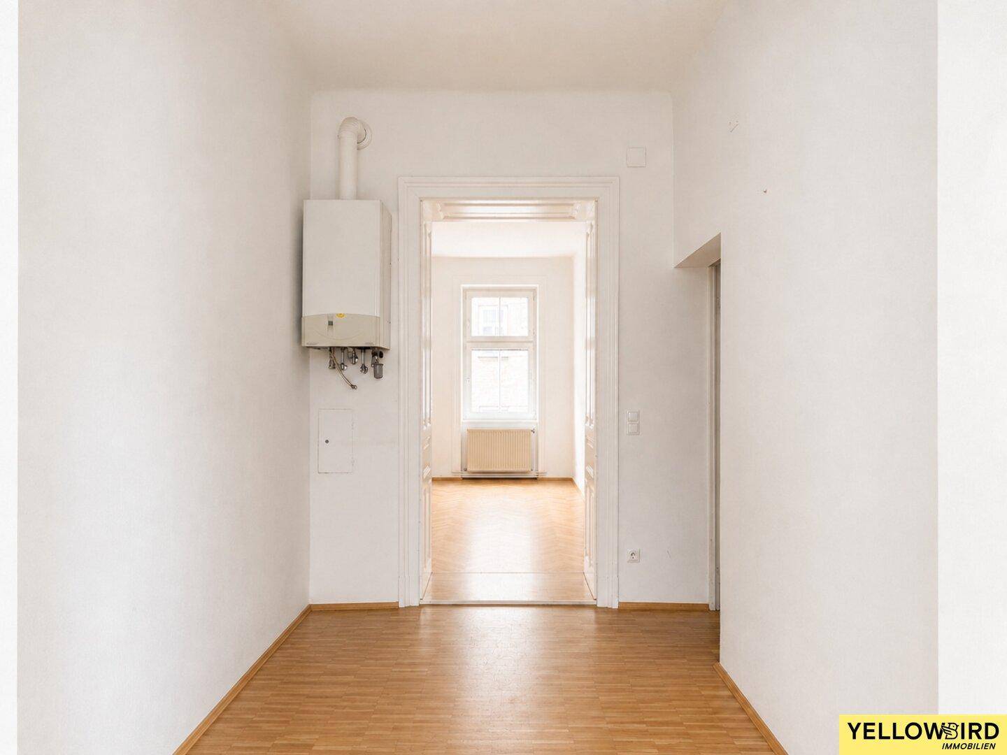Heller Flur mit Holzfußboden und Blick in ein weiteres Zimmer, Gastherme sichtbar.