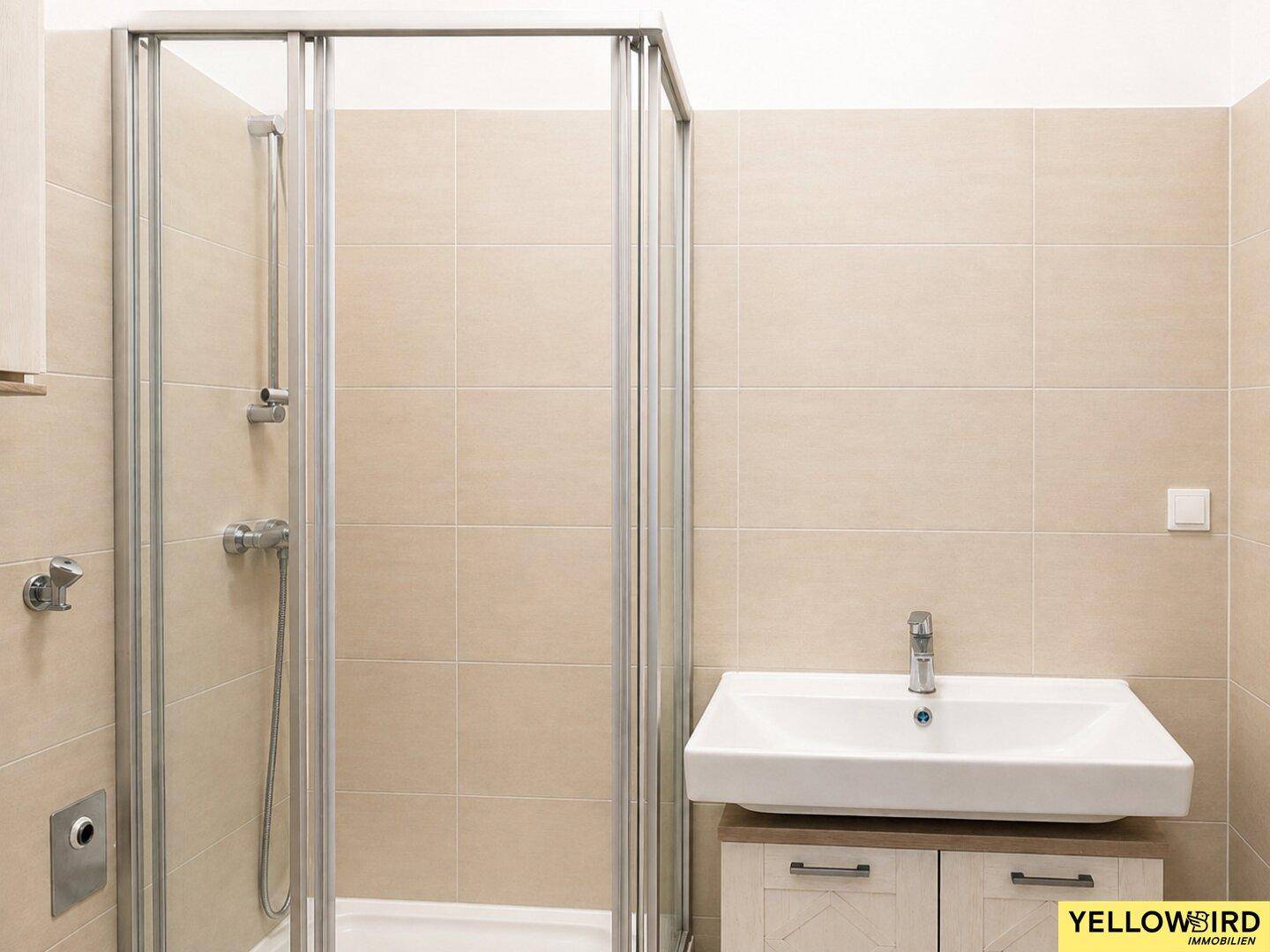Modernes Badezimmer mit beigen Fliesen, Duschkabine und Einzelwaschbecken mit Unterschrank.