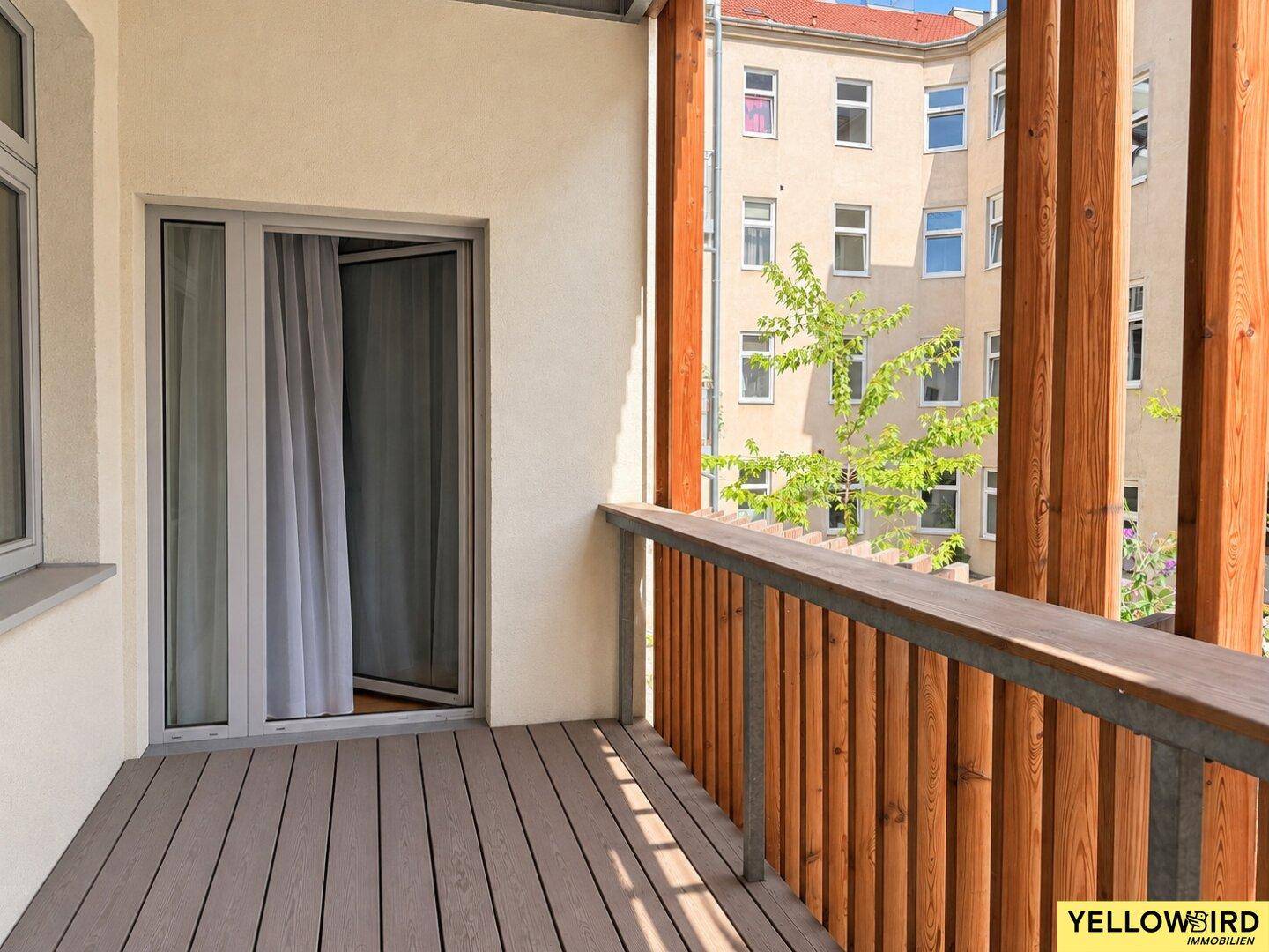 Balkon mit Holzboden und Zugang zum Innenraum, bietet einen ruhigen Blick auf den Innenhof.