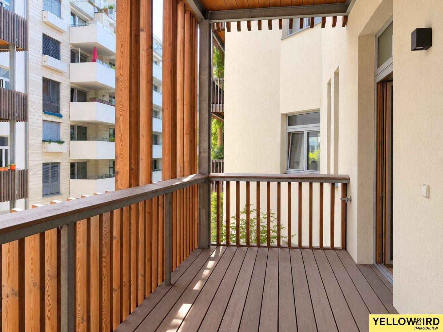 Geräumiger Balkon mit Holzboden und vertikalen Holzlamellen, bietet einen Blick auf umliegende Gebäude.