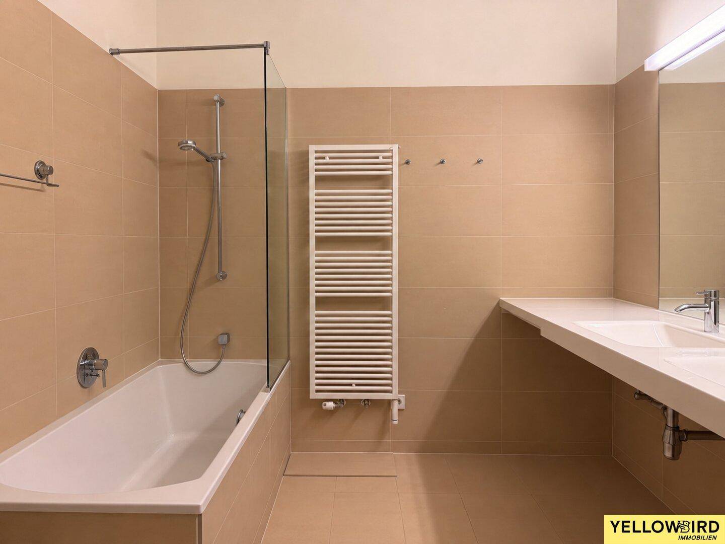 Modernes Badezimmer mit beigefarbenen Fliesen, Badewanne, beheiztem Handtuchhalter und Waschtisch.
