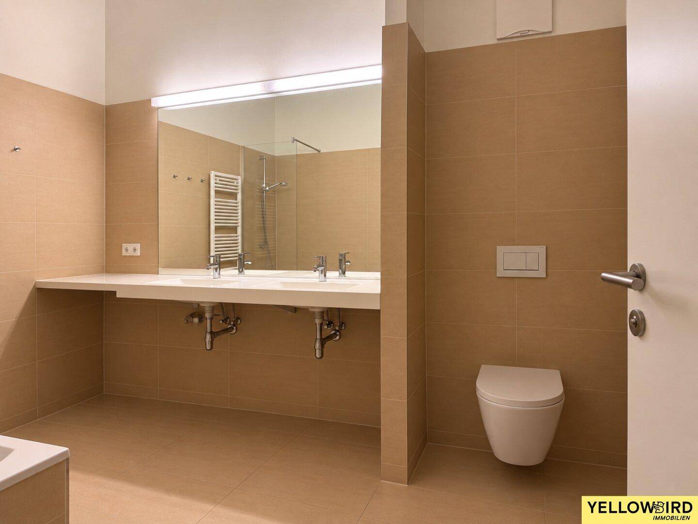 Modernes Badezimmer mit beigefarbenen Fliesen, Doppelwaschbecken, wandhängendem WC und begehbarer Dusche.