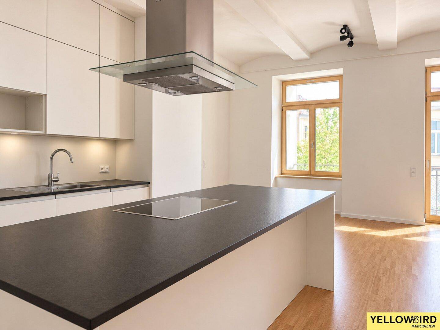 Detailansicht der Kücheninsel mit Induktionskochfeld und moderner Dunstabzugshaube, umgeben von Holzboden.