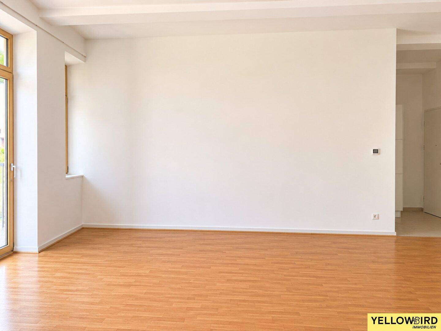 Geräumiges Wohnzimmer mit hellem Holzboden und großen Fenstern, bereit zur individuellen Gestaltung.