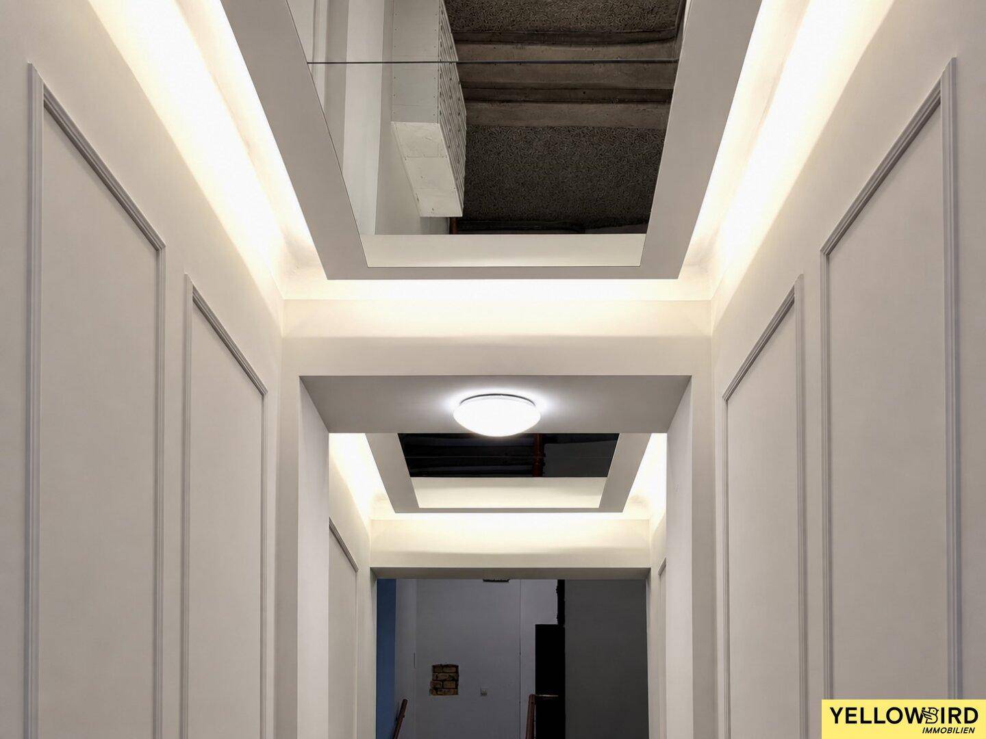 Detailansicht des modernen Deckenlichts im Flur mit architektonischen Elementen und Blick auf das Treppenhaus.