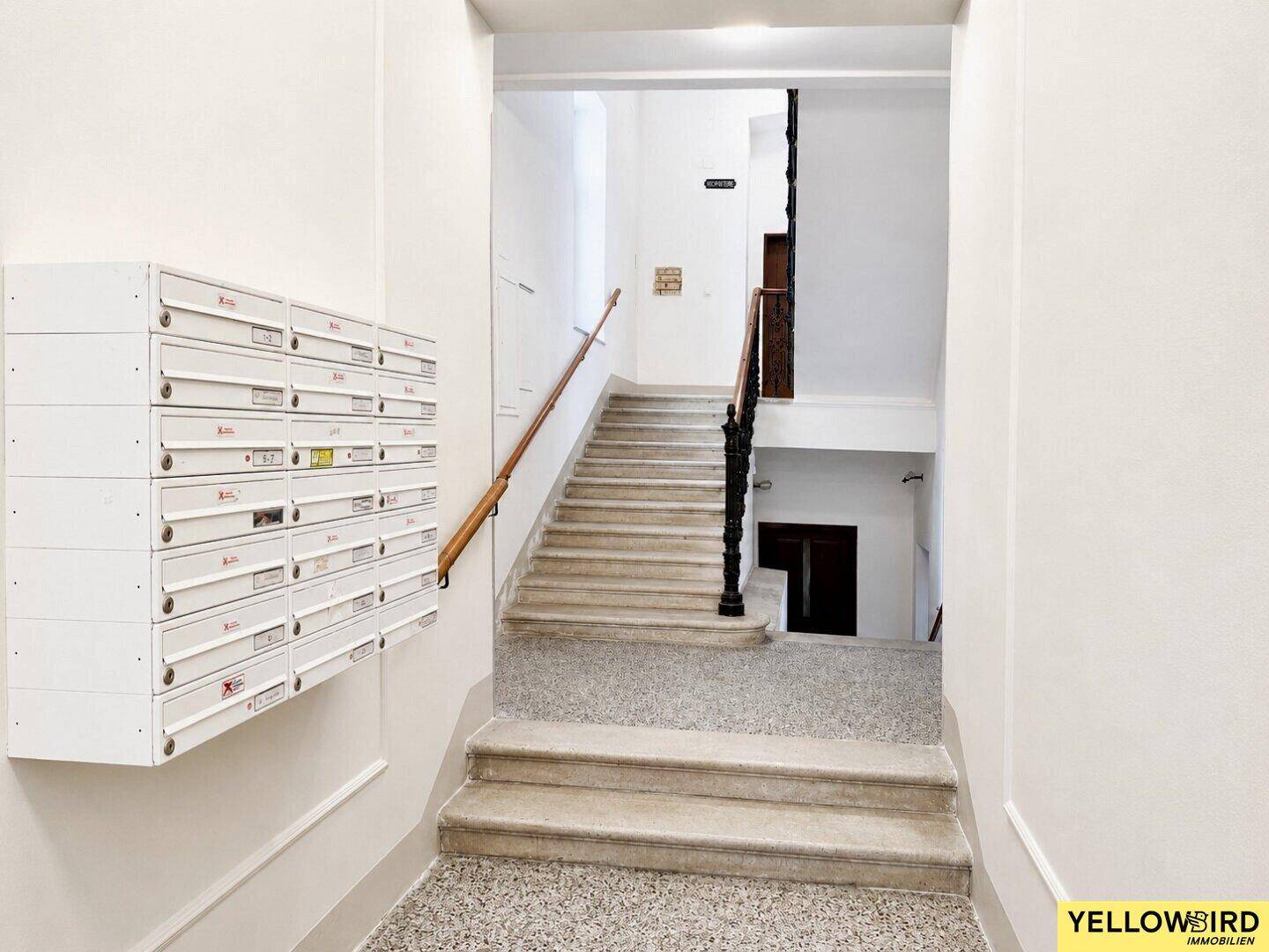 Eingangsbereich mit Briefkästen und einer klassischen Treppe mit schmiedeeisernem Geländer und Holzhandlauf.