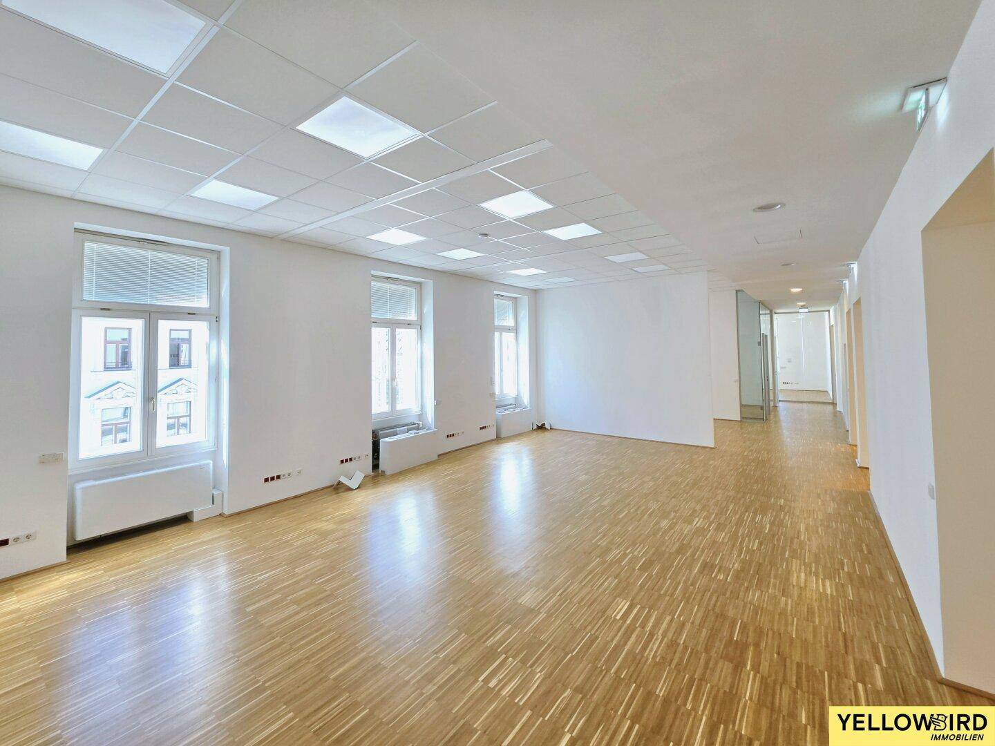 Großer, leerer Büroraum mit Holzparkett und mehreren Fenstern, die viel Licht spenden und eine flexible Nutzung ermöglichen.