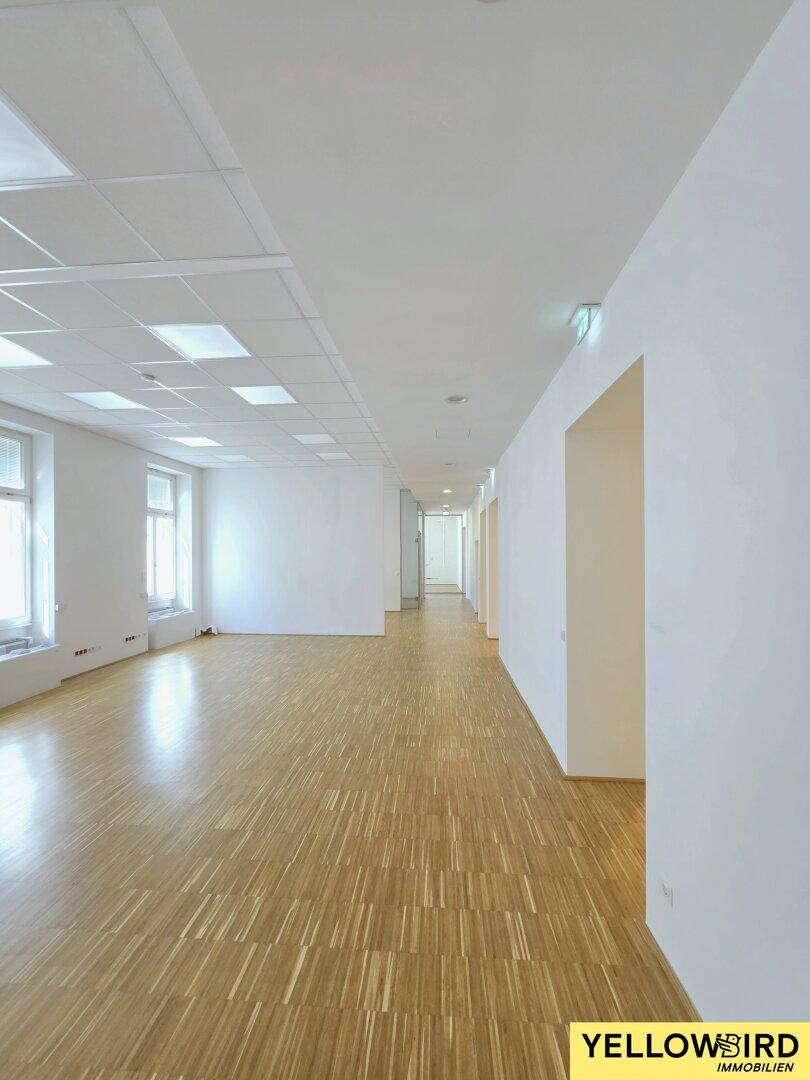 Langer, leerer Büroraum mit Holzparkett und Fenstern, der vielseitig nutzbar ist und viel Platz bietet.