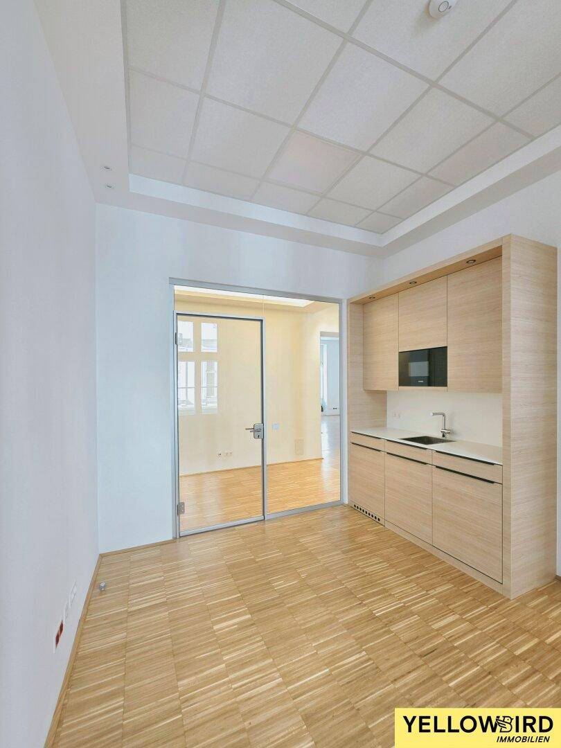 Kleine Küchenzeile mit Holzschränken, Spüle und integrierter Mikrowelle in einem Büroraum, praktisch und funktional.