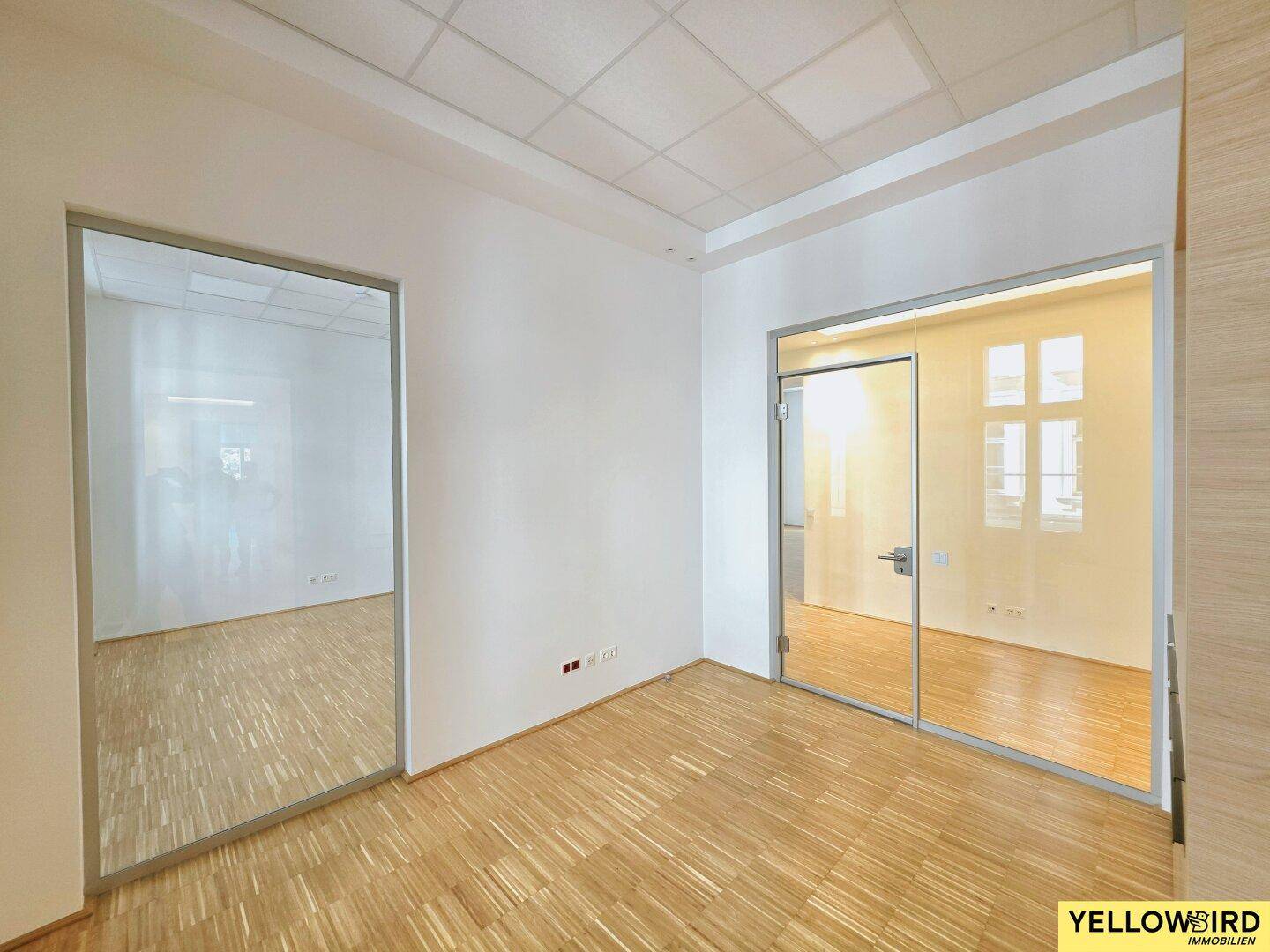 Leerer Büroraum mit Holzparkett und Glaswänden, der vielseitige Gestaltungsmöglichkeiten bietet und hell ist.