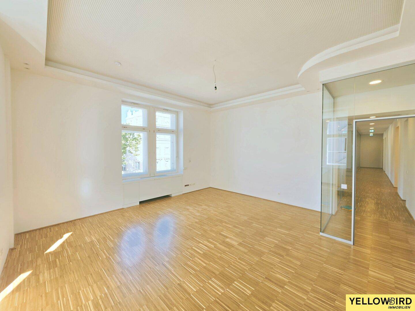 Geräumiger, heller Büroraum mit Holzparkett und großen Fenstern, die viel Tageslicht hereinlassen und eine angenehme Arbeitsatmosphäre schaffen.