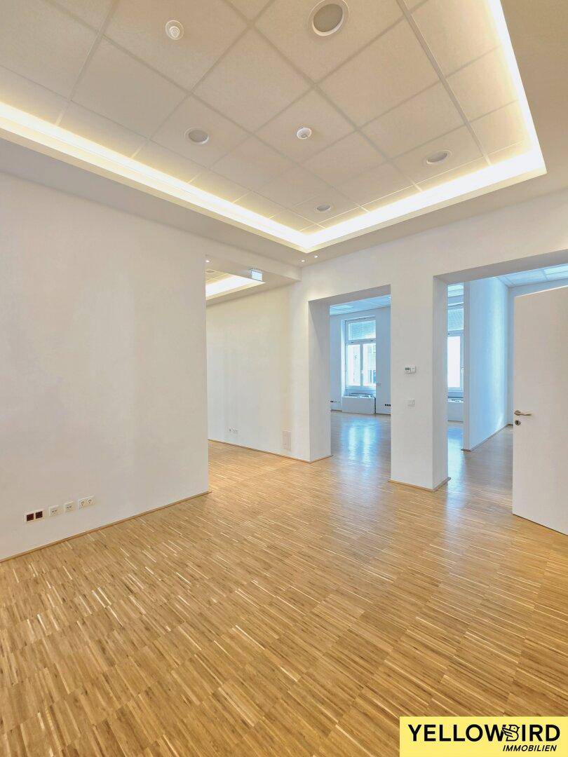 Geräumiger, heller Büroraum mit modernem Holzparkett und indirekter Deckenbeleuchtung, ideal für eine offene Bürogestaltung.