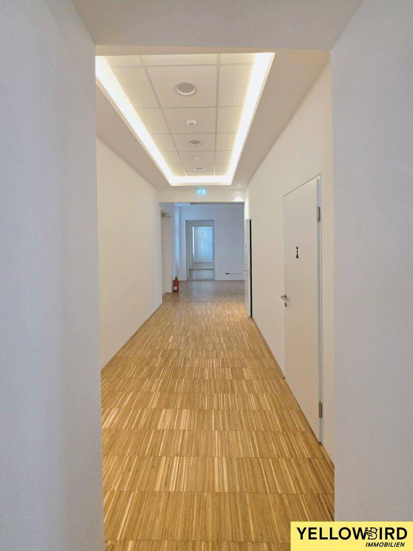 Langer, heller Flur mit Holzparkett und indirekter Deckenbeleuchtung, der zu den Büros führt und einladend wirkt.