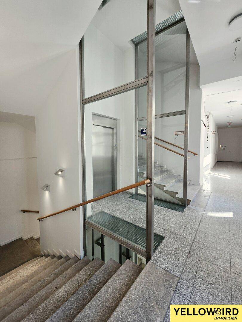 Treppenhaus mit Steinstufen und modernem Aufzug, der die Etagen verbindet und barrierefreien Zugang bietet.