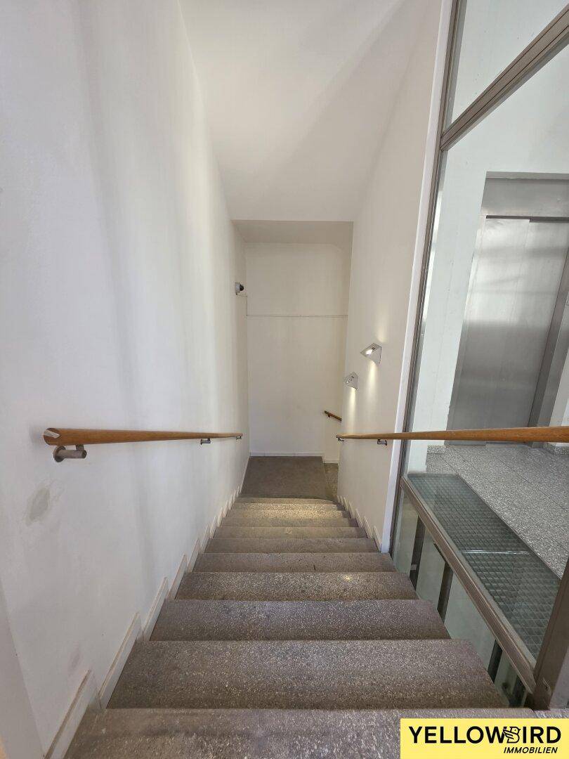 Treppenhaus mit Steinstufen und Holzgeländer, das zu den oberen Etagen führt und robust wirkt.