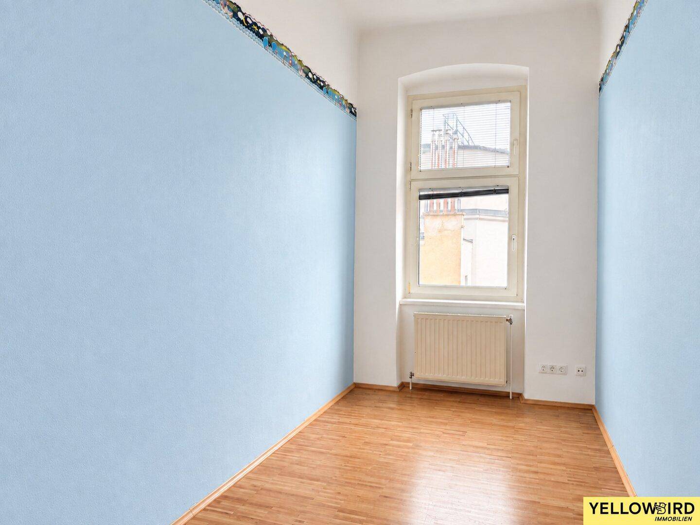 Helles Zimmer mit blauen Wänden, Holzfußboden und einem Fenster mit Ausblick.