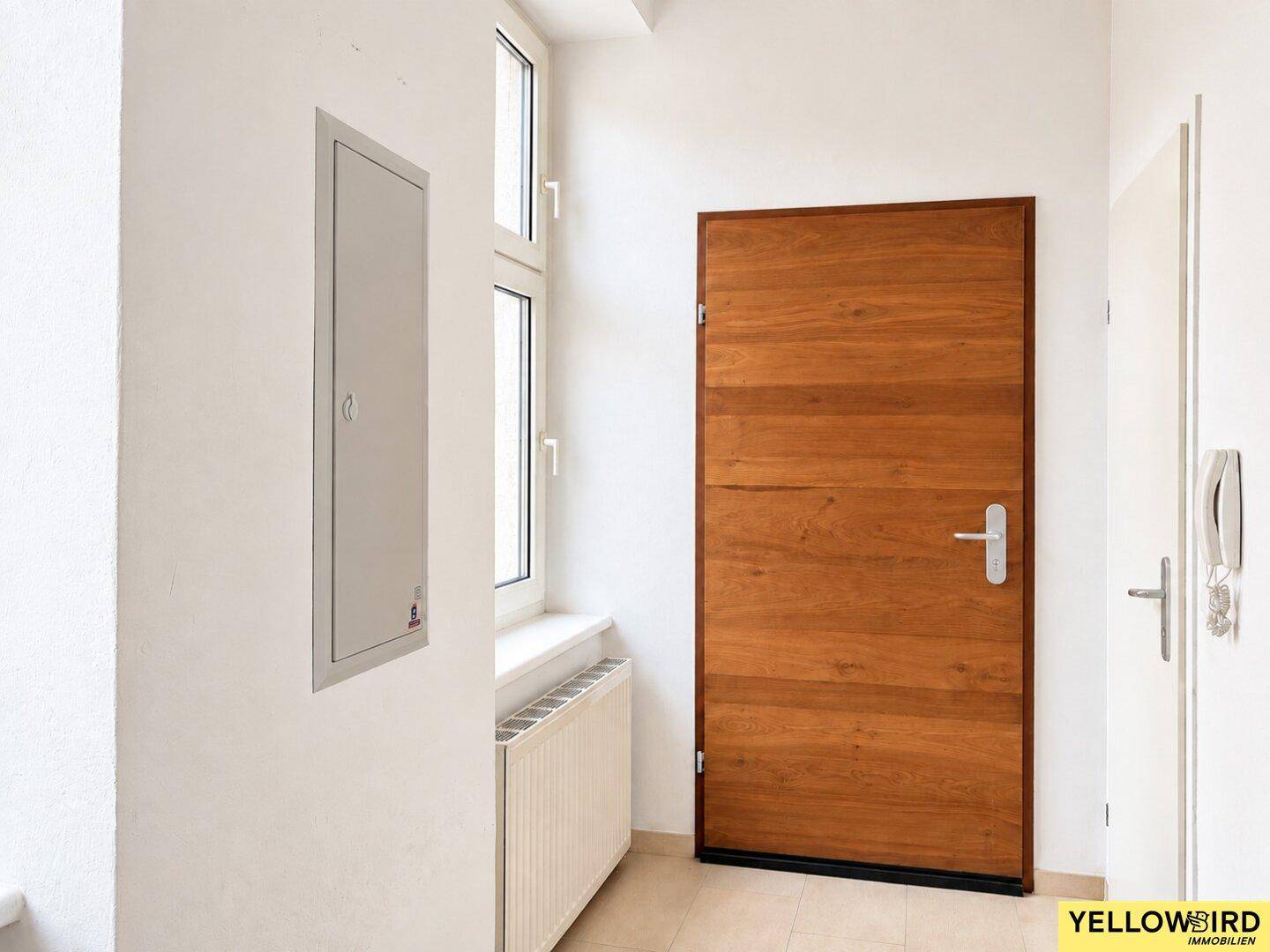 Eingangsbereich mit Holztür, Fliesenboden und einem Fenster für natürliches Licht.