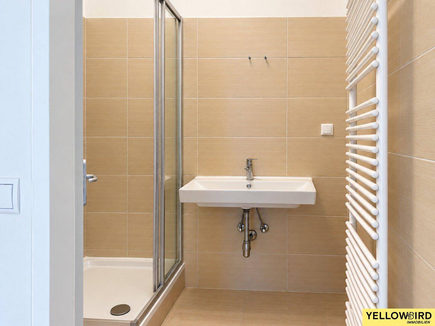 Modernes Badezimmer mit beigefarbenen Fliesen, Dusche und Handtuchheizkörper.