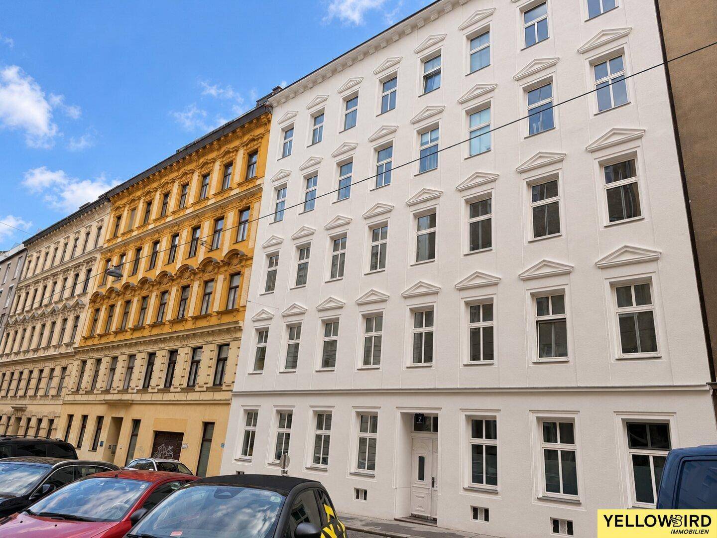 Weiße Fassade eines Mehrfamilienhauses mit vielen Fenstern und klassischer Architektur.