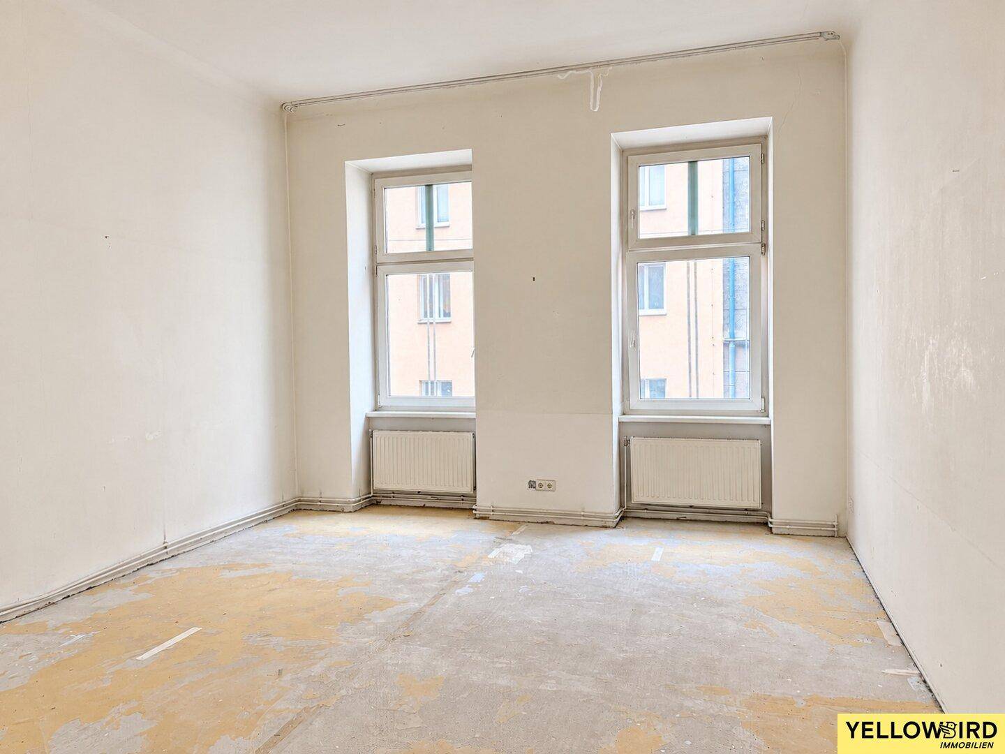 Leerer Raum mit zwei Fenstern und Heizkörpern, bereit für die Renovierung.