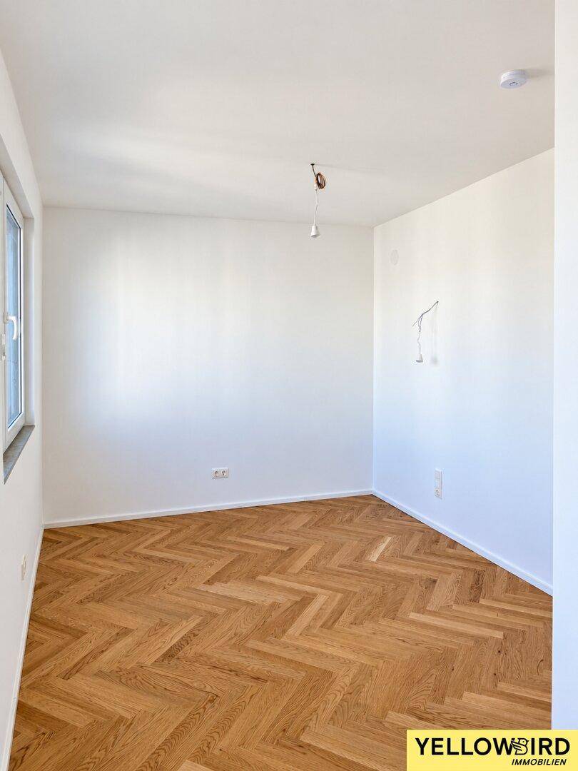 Ruhiges Zimmer mit klassischem Fischgrätparkett und einem Fenster, das viel Tageslicht hereinlässt.