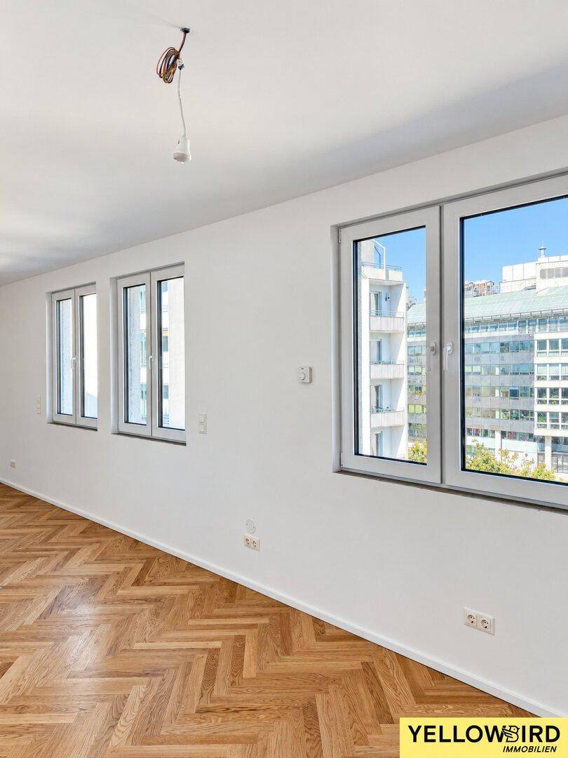 Lichtdurchfluteter Raum mit elegantem Fischgrätparkett und großen Fenstern, die einen weiten Blick auf die Stadt bieten.