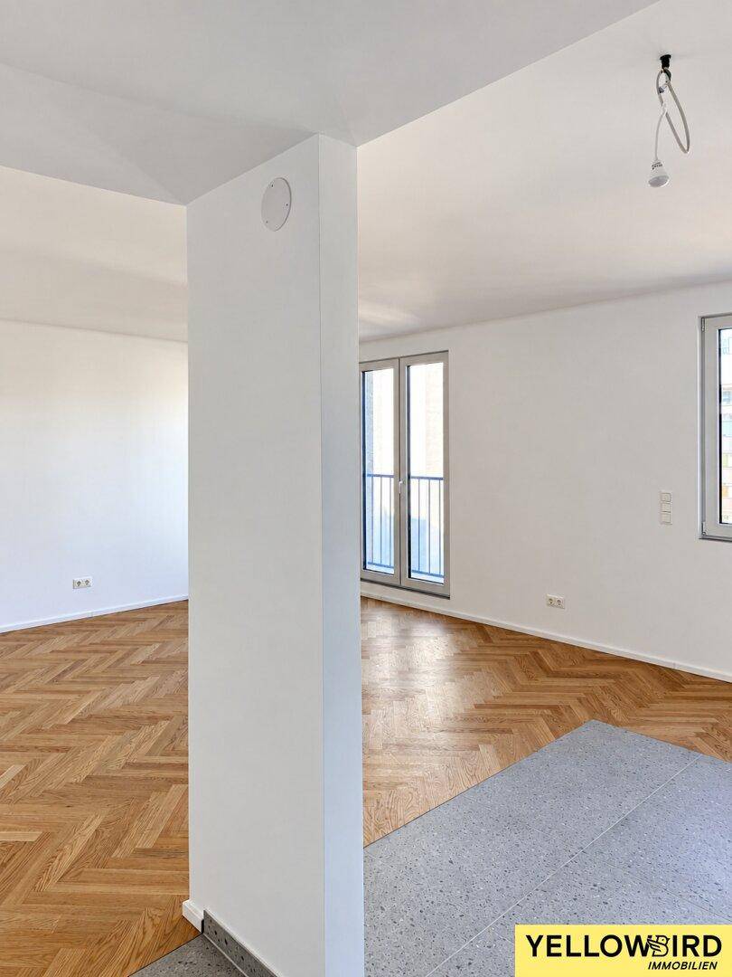 Offener Wohnbereich mit Fischgrätparkett und Fliesenboden, heller Atmosphäre und Zugang zum französischen Balkon.