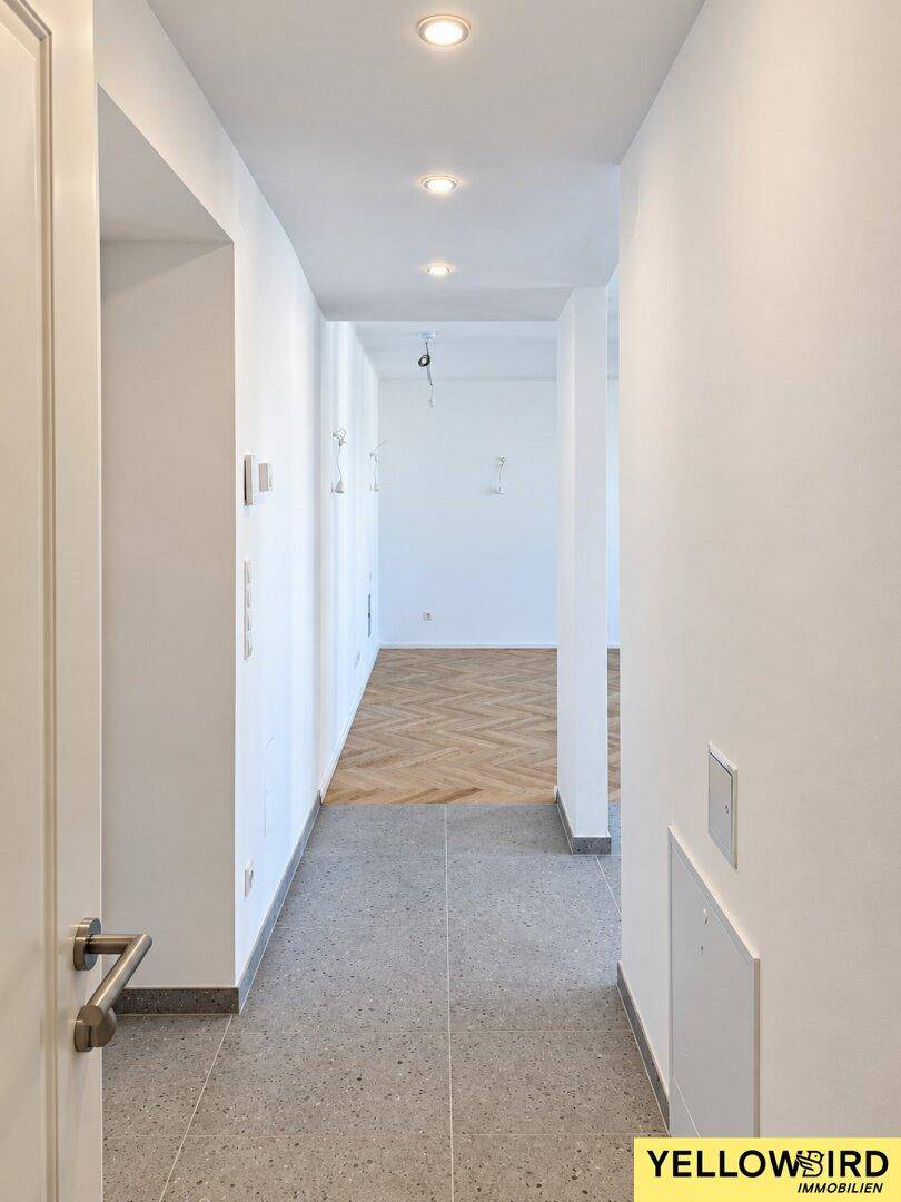 Langer, heller Flur mit modernen grauen Fliesen und Einbaustrahlern, der zu den Wohnbereichen führt.