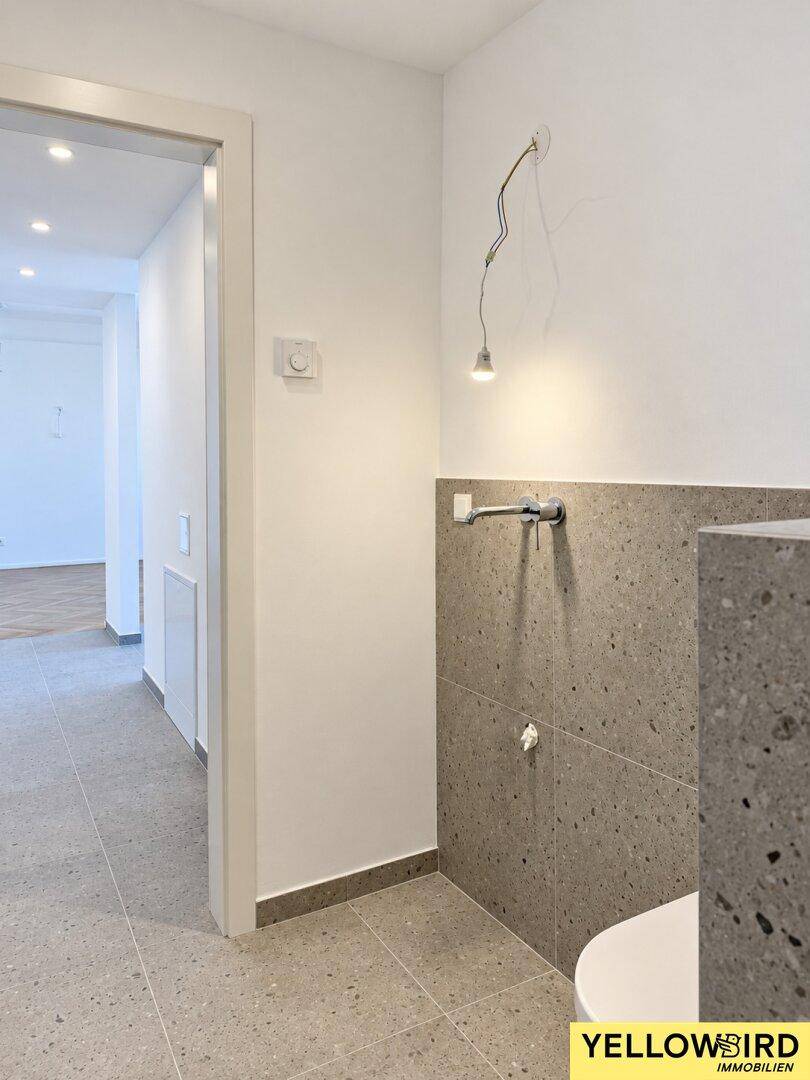 Heller Flur mit modernen grauen Fliesen und Zugang zu einem Badezimmer mit wandhängendem WC.