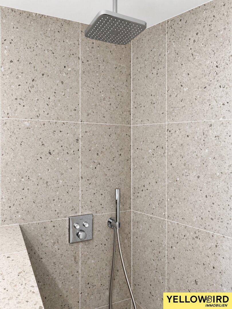 Nahaufnahme des Regenduschkopfs und der modernen Armaturen in der begehbaren Dusche mit grauen Fliesen.
