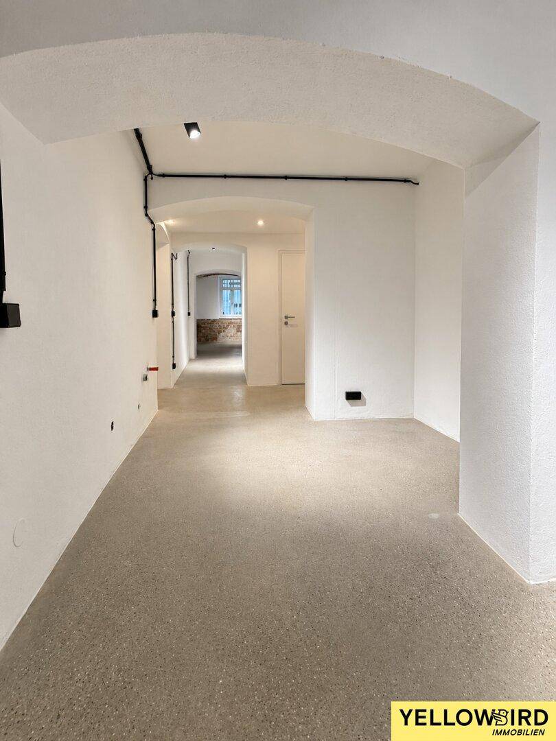 Geräumiger, offener Gewerberaum mit Gewölbedecken und modernem Betonboden, gut beleuchtet.