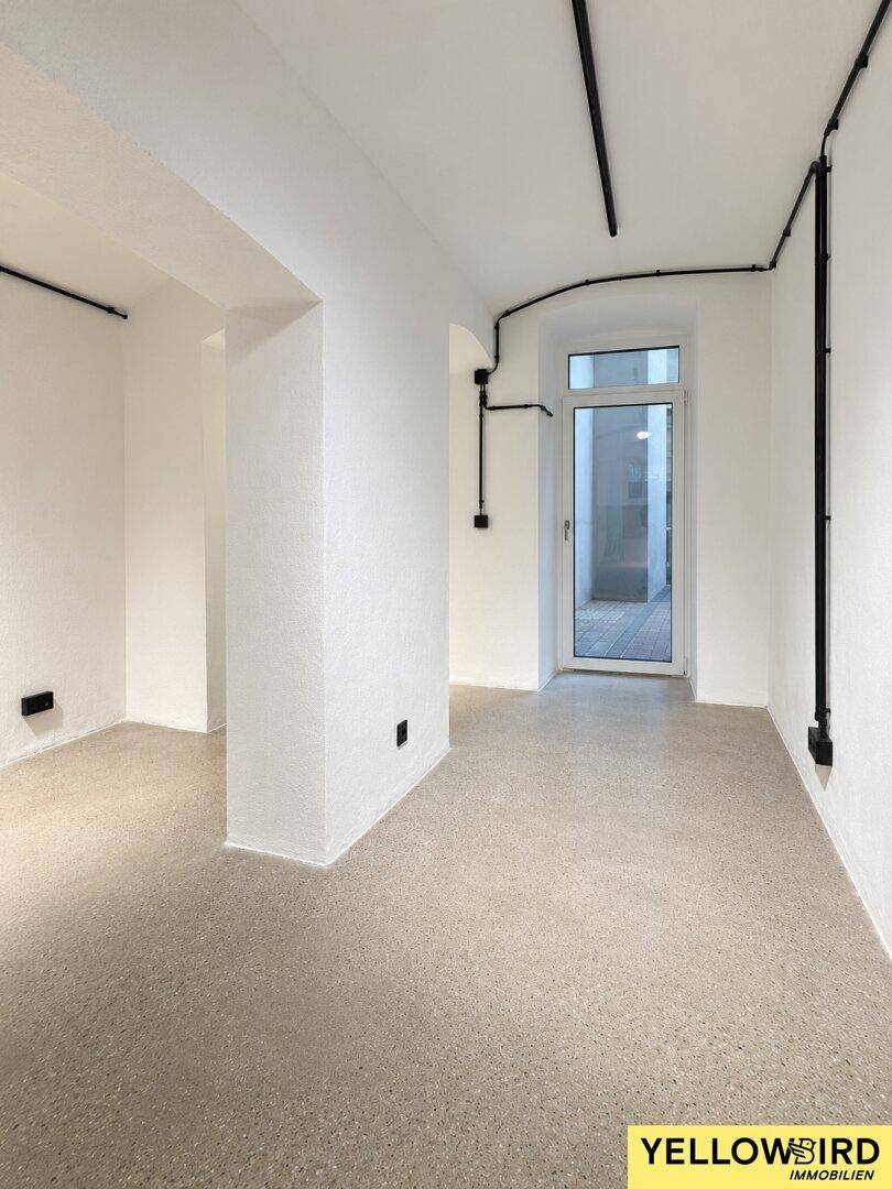 Helle Ecke eines Gewerberaums mit Säule, Betonboden und Zugang zu einem Außenbereich.