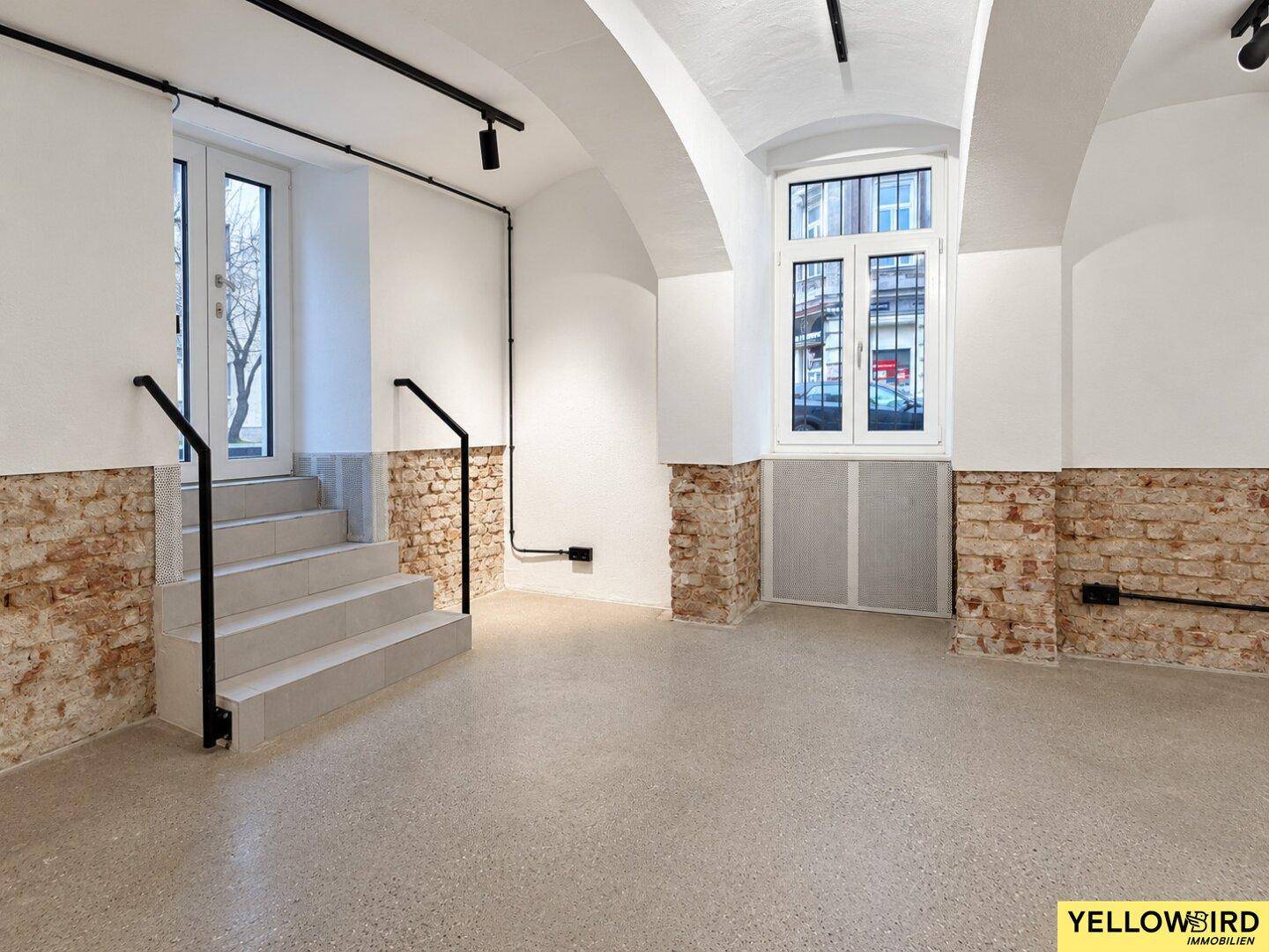 Heller Raum mit Treppe, Gewölbedecke, freigelegten Ziegelwänden und großem Fenster.