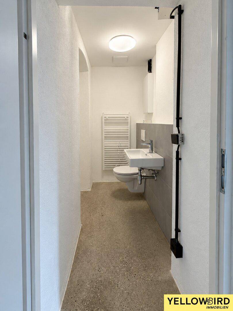 Schmale Gästetoilette mit wandhängendem WC, kleinem Waschbecken und Handtuchheizkörper.