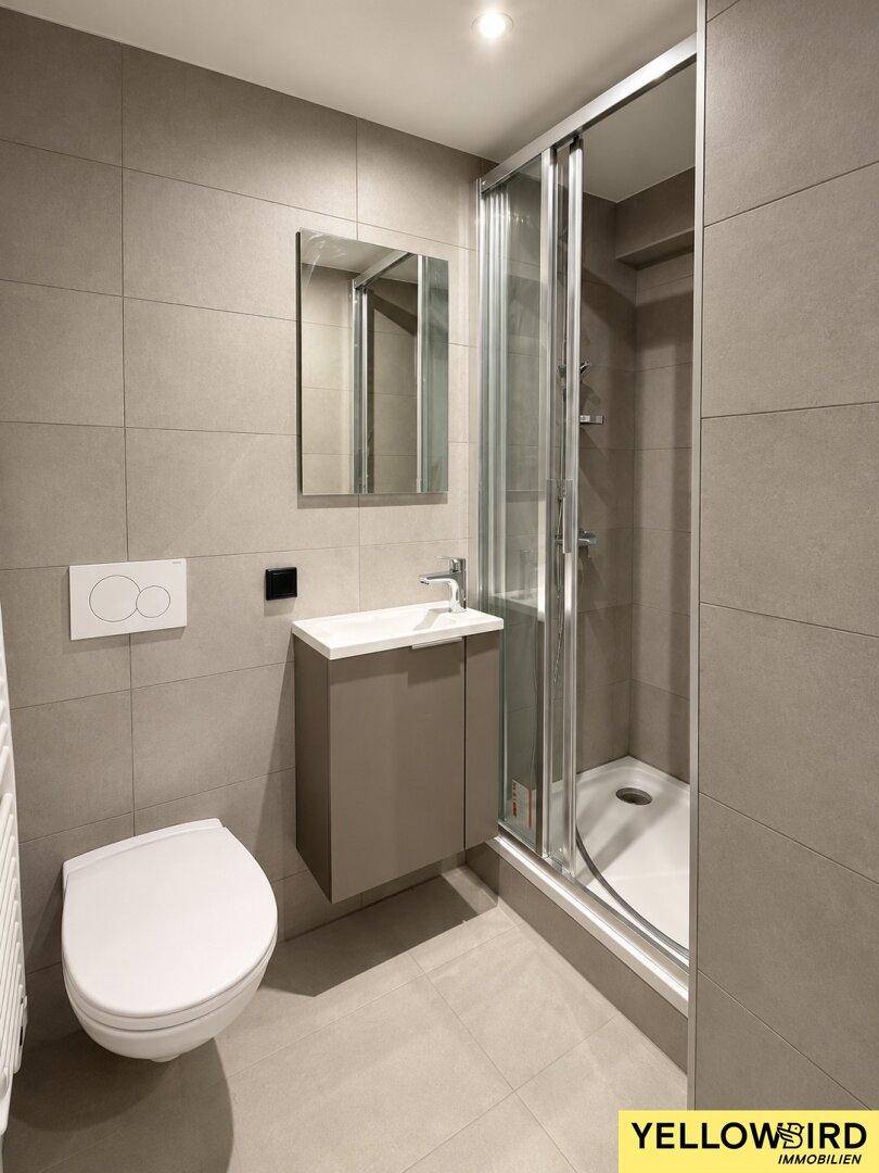 Modernes Badezimmer mit Duschkabine, wandhängendem WC, Waschtisch und großformatigen Fliesen.
