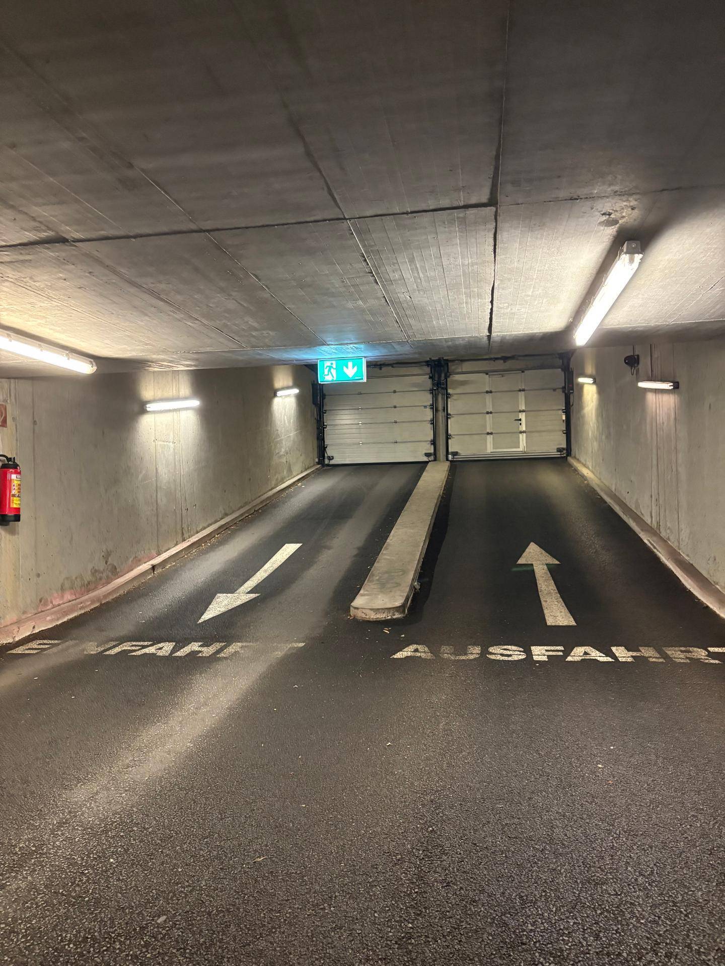 Einfahrt und Ausfahrt einer Tiefgarage mit Rolltoren, Rampe und Beleuchtung.