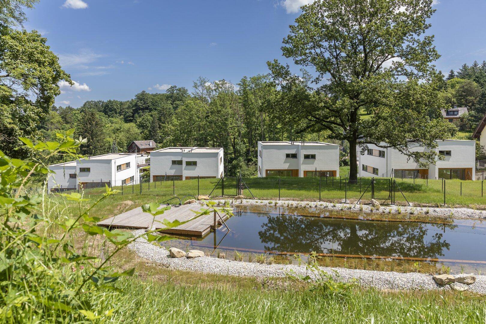 Moderne Wohngebäude in ländlicher Umgebung mit einem natürlichen Teich und viel Grün.