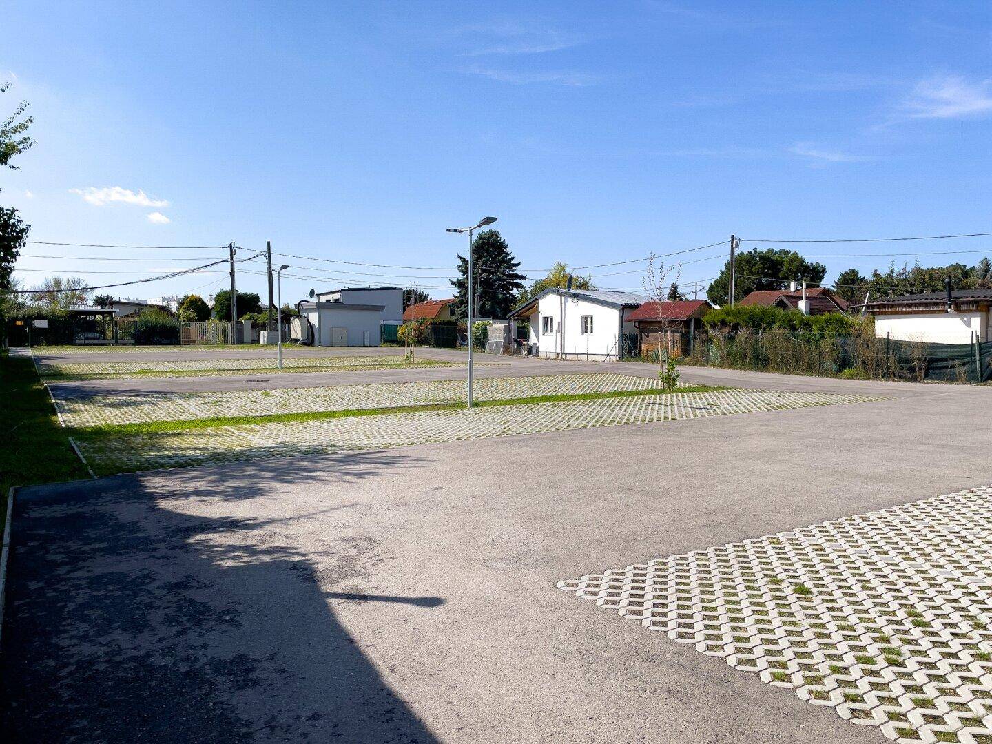 Großer Parkplatz mit Rasengittersteinen und umliegender Bebauung unter klarem Himmel.