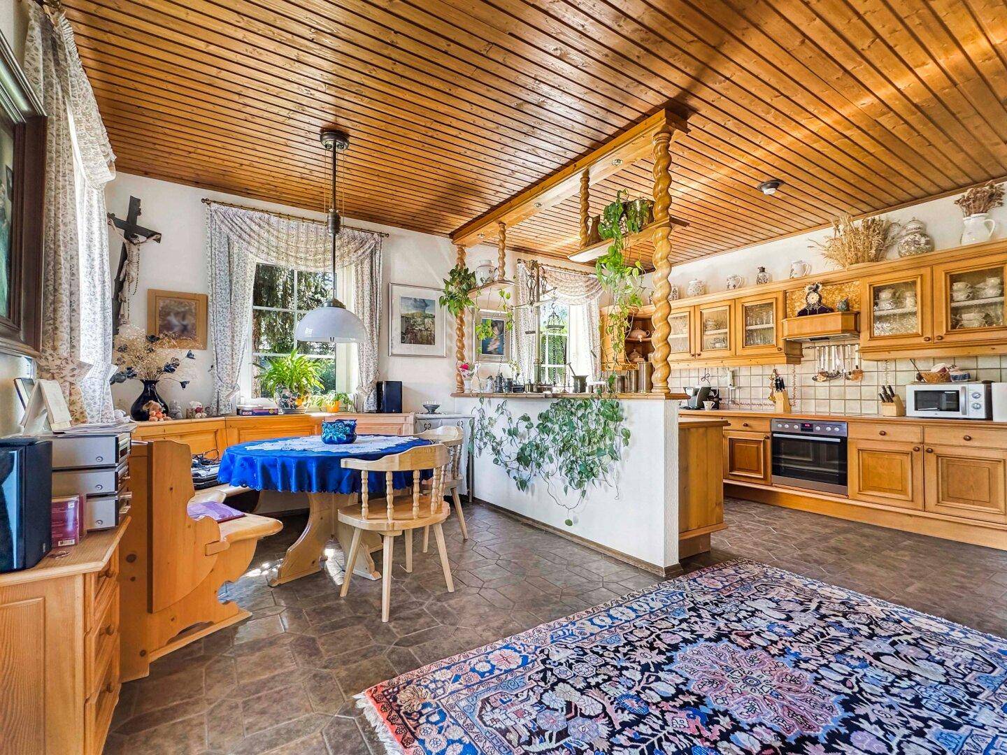 Geräumige Wohnküche mit Holzmöbeln, Essbereich und Blick in den Garten durch große Fenster.