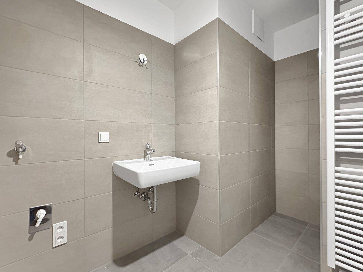 Modernes Badezimmer mit grauen Fliesen, wandhängendem Waschbecken und beheiztem Handtuchhalter.