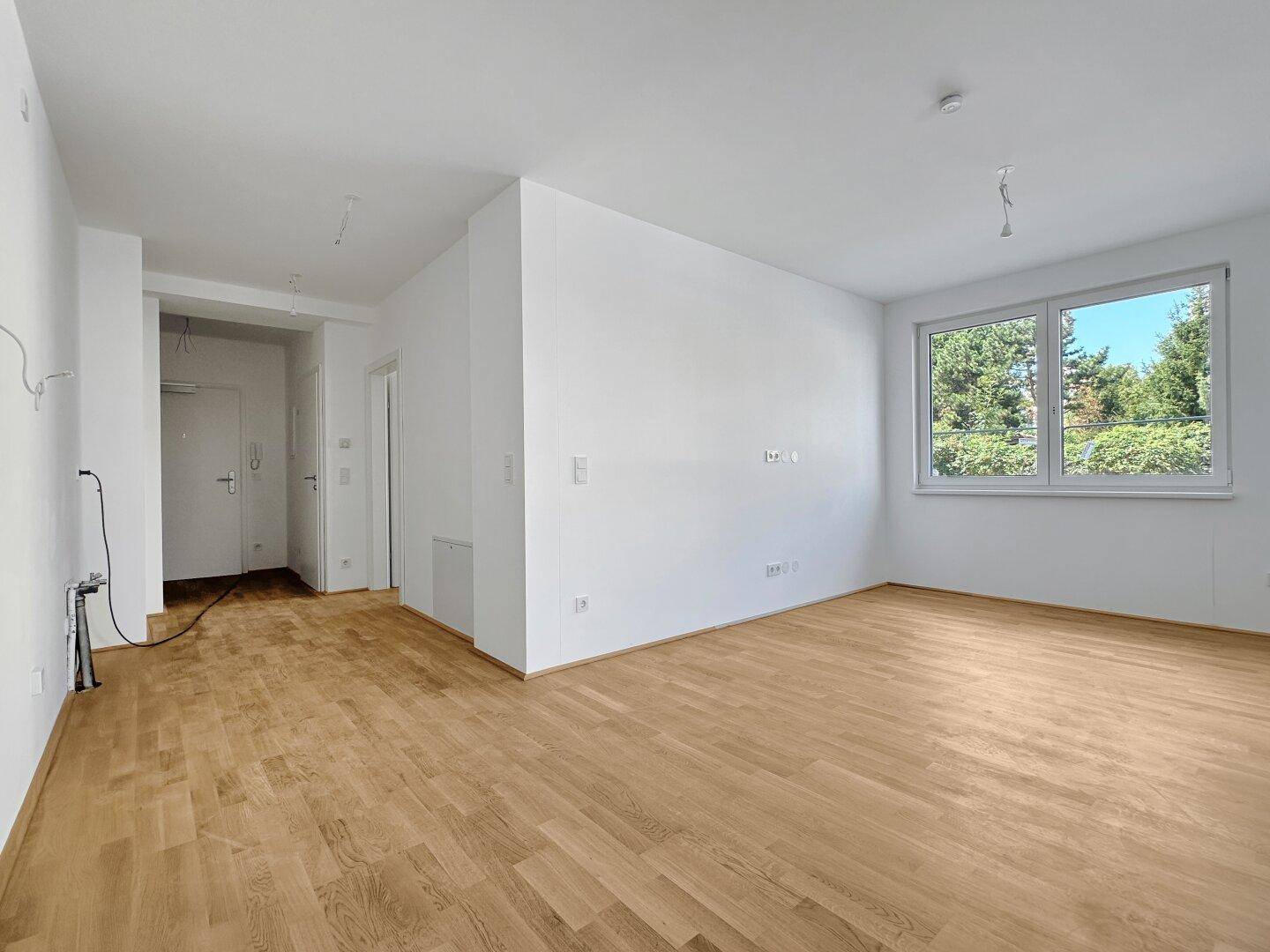Geräumiges, helles Zimmer mit Holzboden und großen Fenstern, die einen Blick ins Grüne bieten.