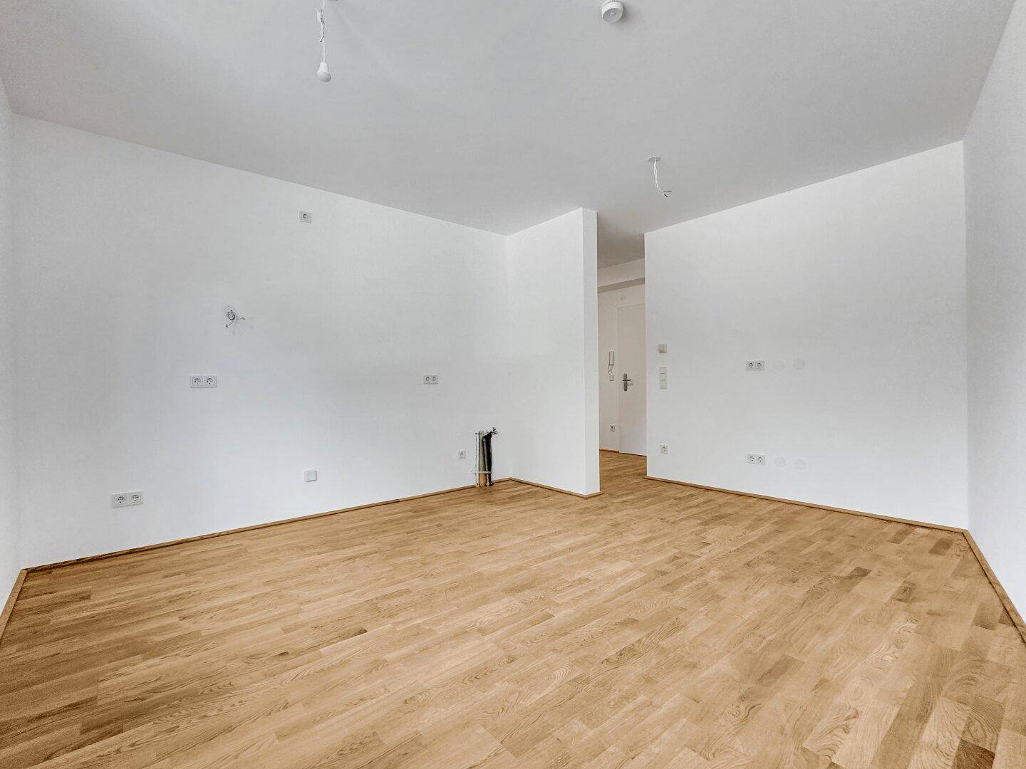 Geräumiger, heller Raum mit Parkettboden und offenem Zugang zu einem weiteren Bereich der Wohnung.