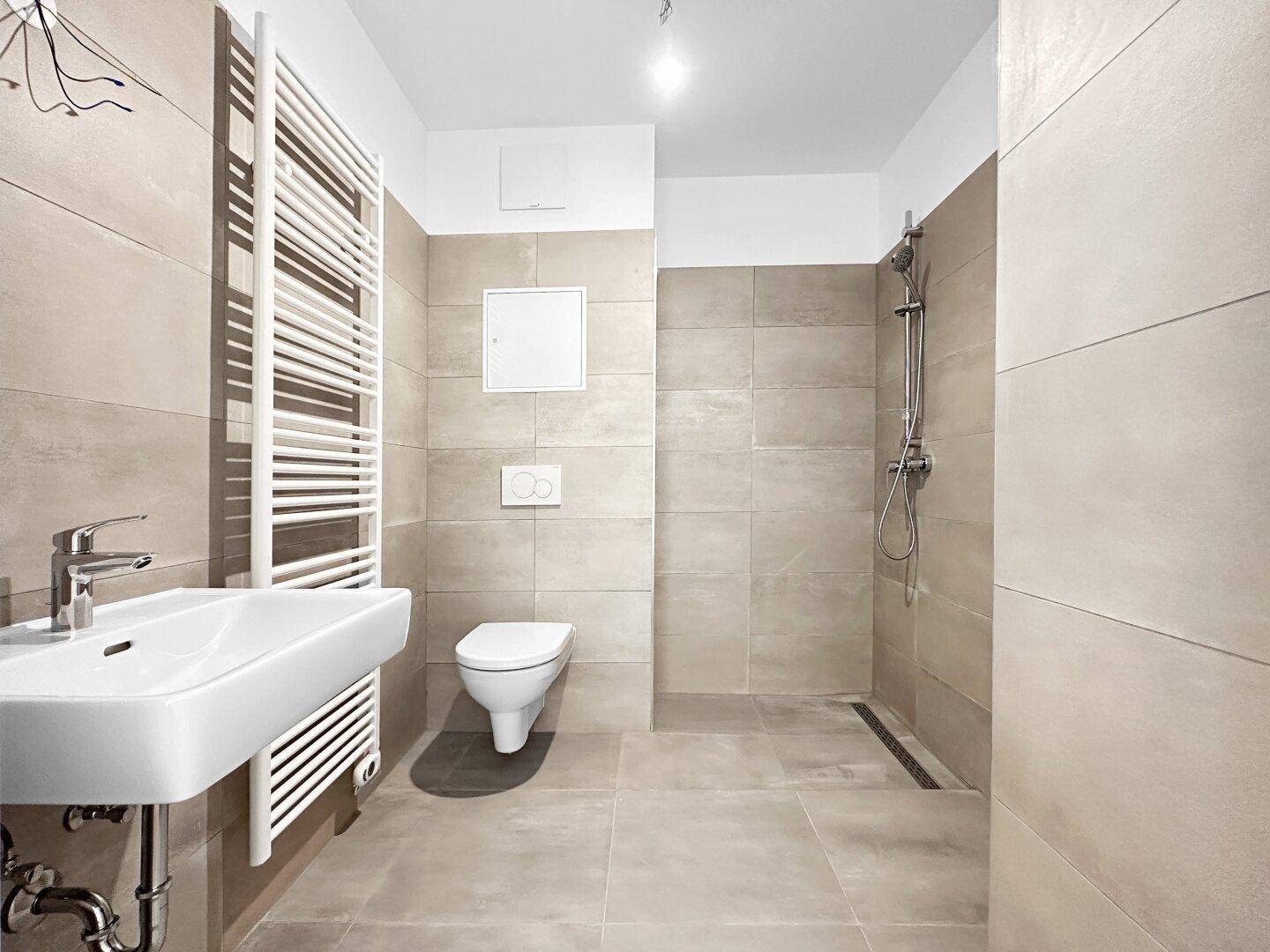 Modernes Badezimmer mit beigefarbenen Fliesen, ebenerdiger Dusche und Wand-WC.