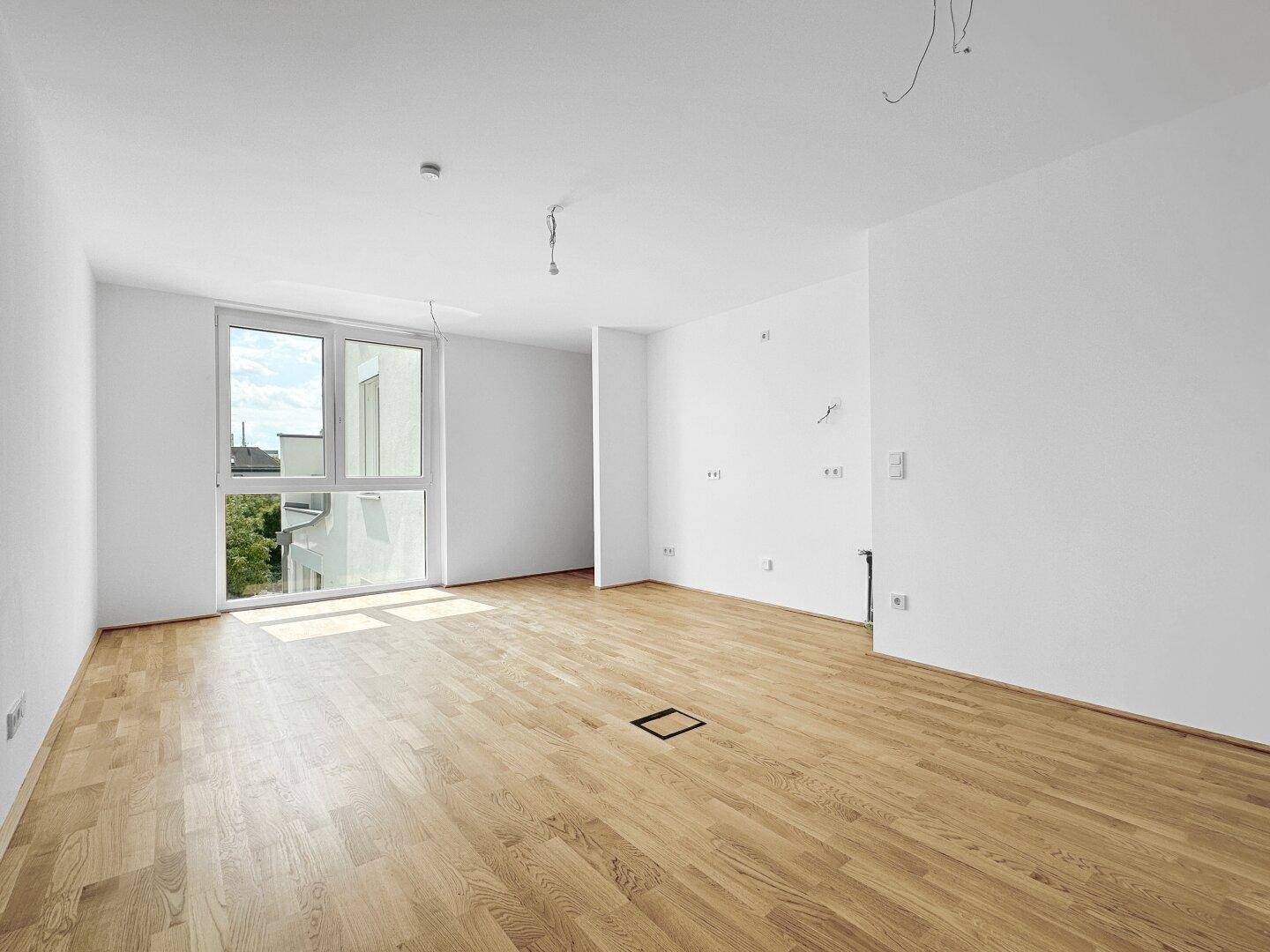 Helles, leeres Zimmer mit Parkettboden und großem Fenster, bereit zur individuellen Gestaltung.