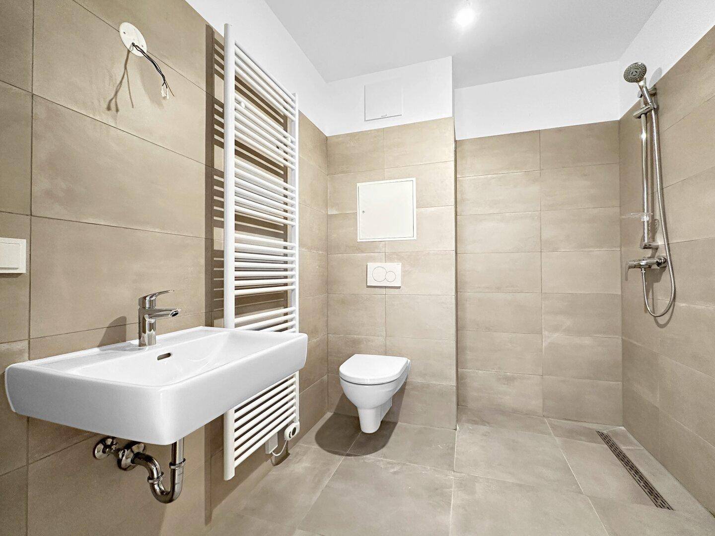 Modernes Badezimmer mit beigen Fliesen, wandhängendem WC und ebenerdiger Dusche.