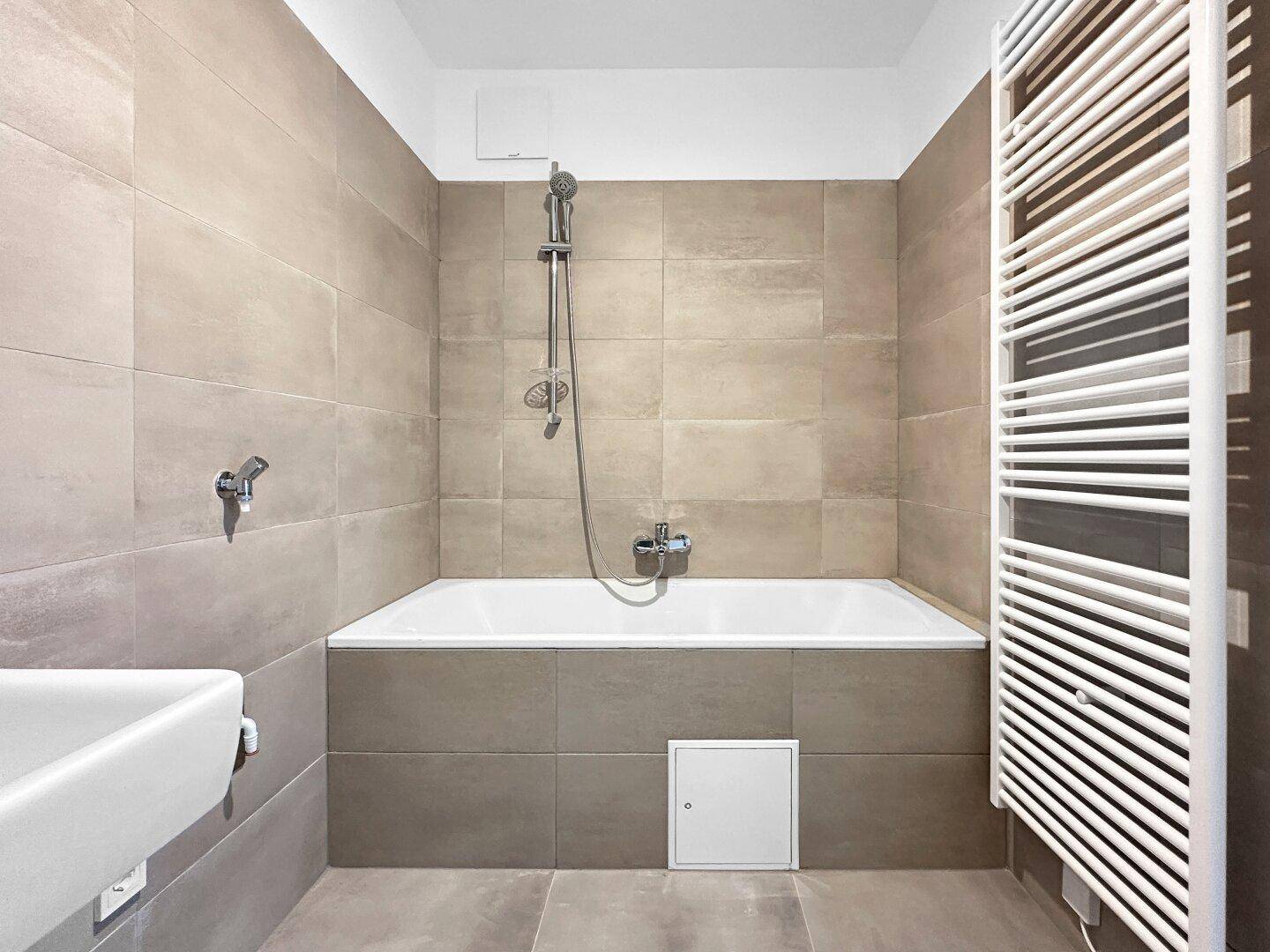 Modernes Badezimmer mit Badewanne, beigefarbenen Fliesen und einem beheizten Handtuchhalter.